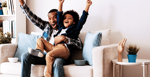 Father and Son Sitting Down in living room and Cheering