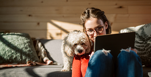 Woman browsing a tablet on a couch while her dog watches