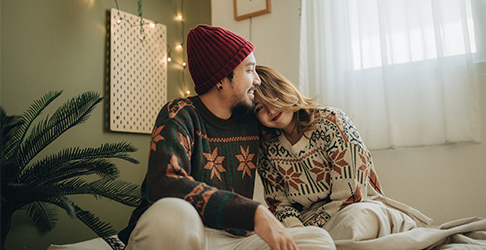 Cozy couple in sweaters lean on each other in their house while seated
