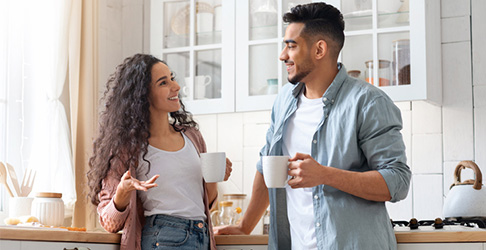 Husband and wife in a kitchen chatting over a cup of coffee